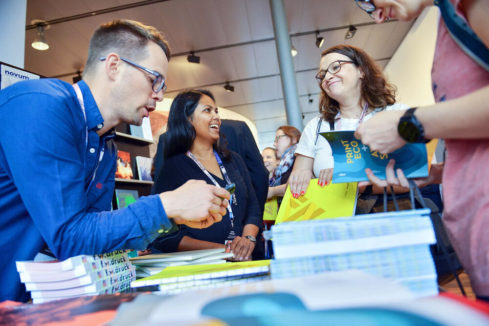 Mehrere Menschen unterhalten sich an einem Tisch mit vielen Print Produkten